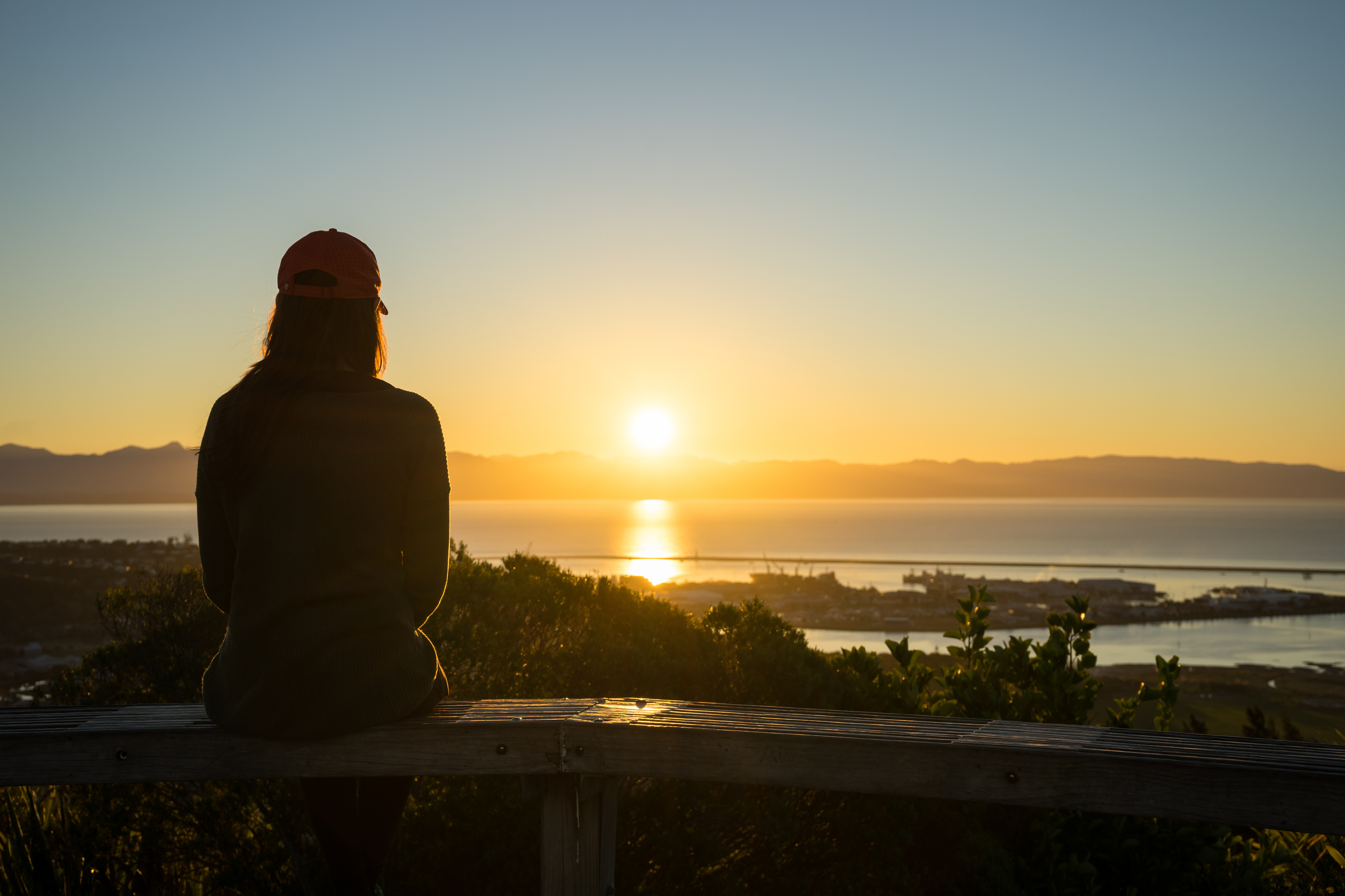 Person sitting alone watching the sunset over the hills, sea, and harbour in New Zealand